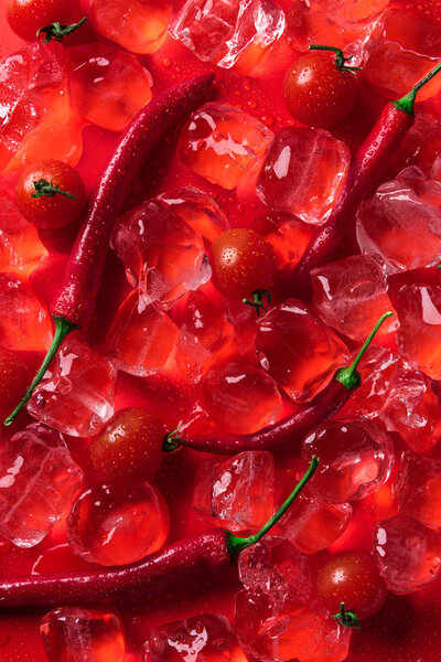 top view of ice cubes, cherry tomatoes and chili peppers on red surface