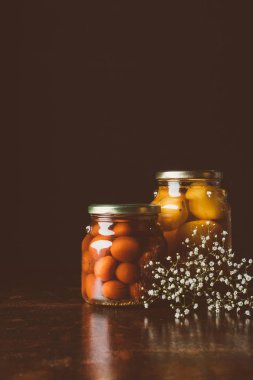 glass jars with preserved tomatoes on wooden table in dark kitchen  clipart