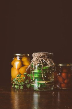 glass jars with preserved vegetables on wooden table in dark kitchen  clipart