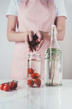 cropped image of woman putting tomatoes in glass jar with water at kitchen clipart