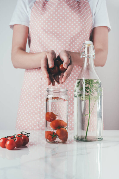 cropped image of woman putting tomatoes in glass jar with water at kitchen
