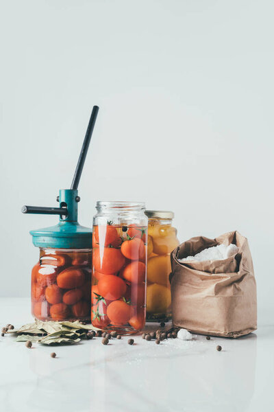 glass jars and tool for preserving tomatoes on table in kitchen