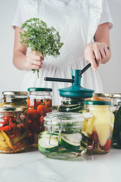 cropped image of woman preparing preserved vegetables in glass jars at kitchen