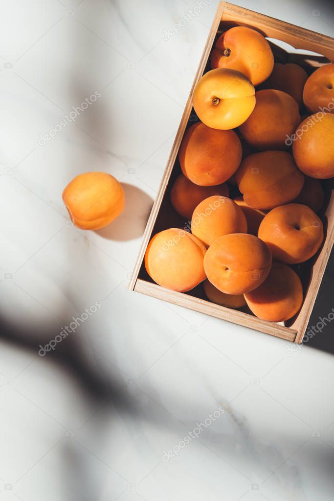 flat lay with ripe apricots in wooden box on light marble surface