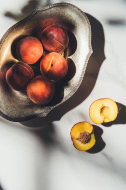 flat lay with ripe peaches in metal bowl on light marble surface with shadows clipart