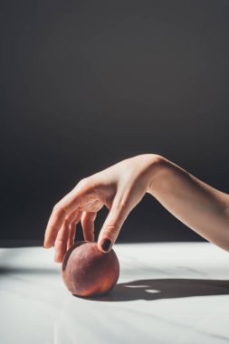 partial view of woman holding ripe peach in hand on black background clipart