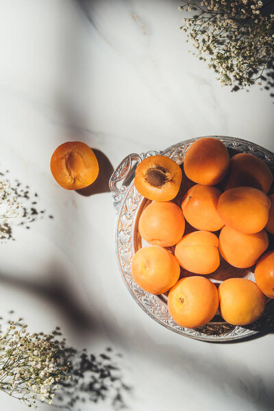 flat lay with ripe apricots on metal tray with gypsophila flowers on light marble tabletop with shadows