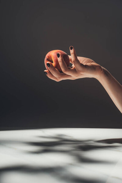 partial view of woman holding ripe peach in hand on black background