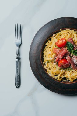 makarna nane ile yükseltilmiş görünümünü bırakır, jamon ve kiraz domates parmesan tarafından plaka mermer masada çatal ile kaplı 