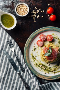 Nane yaprakları, jamon ve mutfak havlusu, bıçak, çatal, çam fıstığı ve pesto kase masada plaka üzerinde parmesan tarafından örtülü domates makarna üstten görünüm 