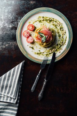 Nane yaprakları, jamon, çam fıstığı, pesto ve bıçak, çatal ve Mutfak havlu ile masada tabakta rendelenmiş parmesan kapsadığı domates makarna üstten görünüm 