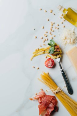 zeytinyağı ve jamon masada çatal üstten görünüm çevrili çam fıstığı, pesto, parmesan, pişmemiş spagetti, cherry domates, tuz, makarna tarafından sarılmış 