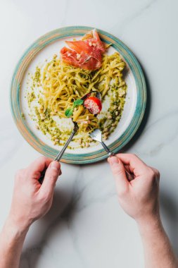 man yemek makarna nane yaprakları, jamon, çam fıstığı, pesto ve kiraz domates rendelenmiş parmesan mermer masada kapsadığı kırpılmış görüntü 
