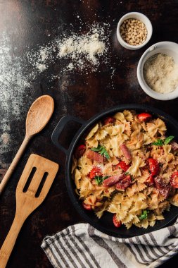 jamon, çam fıstığı, sos, domates, mutfak havlusu, tahta spatula ve tablo kaşık çevrili tavada rendelenmiş parmesan kapsadığı nane yaprakları ile makarna üstten görüntülemek 