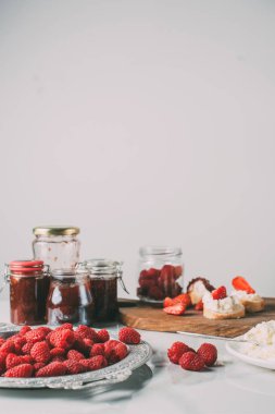 selective focus of raspberries and jars with fruit jam on grey clipart