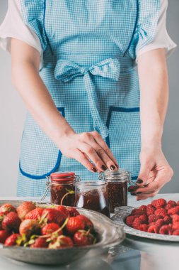 partial view of woman doing jam from strawberries and raspberries at kitchen  clipart