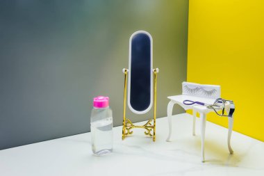 toy mirror and dressing table with bottle of lotion and eyelash curler in miniature room clipart