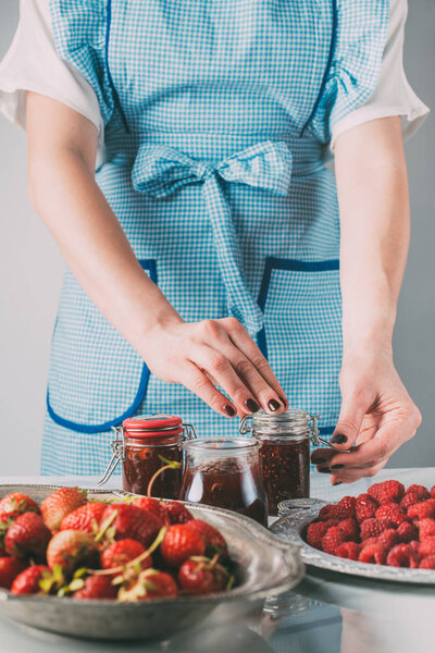 partial view of woman doing jam from strawberries and raspberries at kitchen 