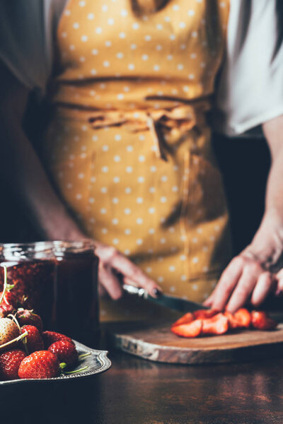 cropped image of woman in apron cutting strawberries at table 