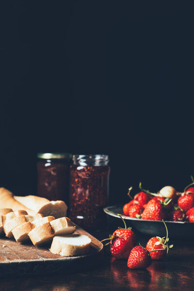 close up view of strawberries in silver tray, flowers and jam in jars on black 