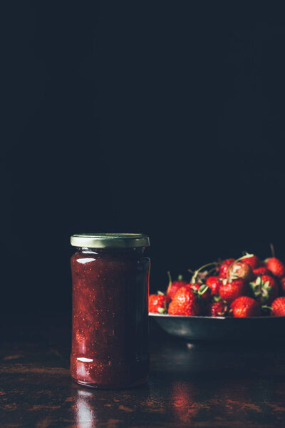 selective focus of jar with strawberry jam and silver tray with strawberries on black 