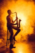 fiatal profi zenész ül a széken, és játék a saxophone füst 