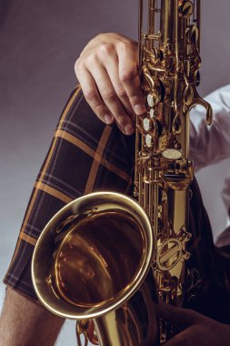 close-up partial view of stylish professional musician holding saxophone on grey clipart