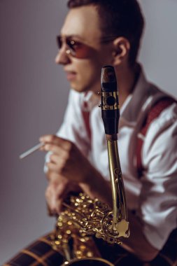 selective focus of young saxophonist smoking cigarette on grey clipart