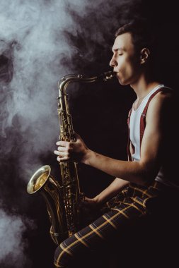 oturma ve siyah duman saksafon oynamaya şık genç jazzman yan görünüm 