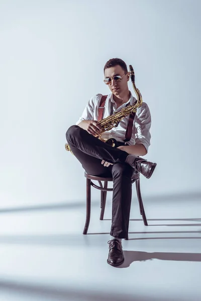Stijlvolle Jonge Performer Zonnebril Zittend Een Stoel Bedrijf Saxofoon Grijs — Stockfoto
