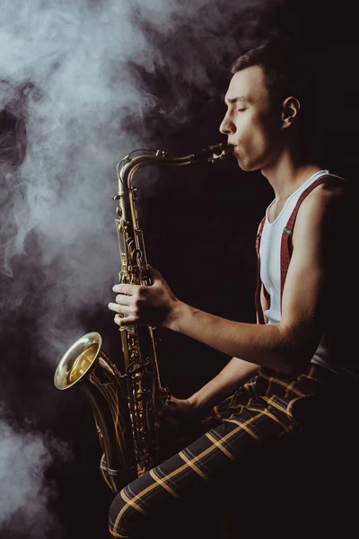 Vista Lateral Elegante Jovem Jazzman Sentado Tocando Saxofone Fumaça Preto — Fotografia de Stock