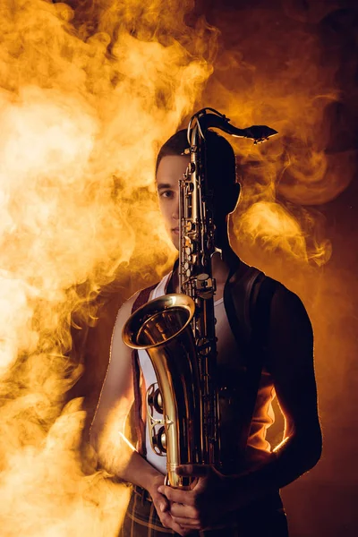 Joven Músico Masculino Sosteniendo Saxofón Mirando Cámara Humo — Foto de stock gratis