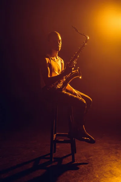 Jovem Jazzman Olhando Para Câmera Enquanto Sentado Fezes Segurando Saxofone — Fotografia de Stock Grátis