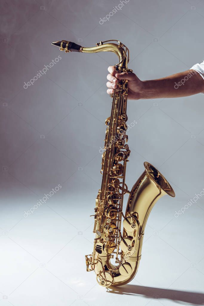 close-up partial view of man holding saxophone in smoke on grey