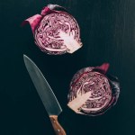 Top view of cut red cabbage and knife on grey dark table