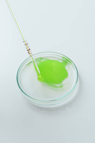 close-up shot of green liquid pouring from pipette into petri dish