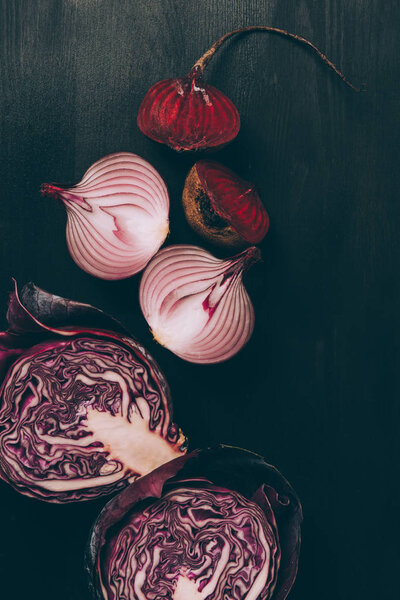 elevated view of halves of beetroot, onion and red cabbage on grey dark table 
