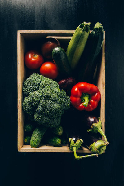 top view of zucchini, broccoli and eggplants in wooden box on dark table