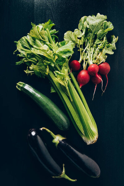 top view of celery, radishes and eggplants on grey dark table