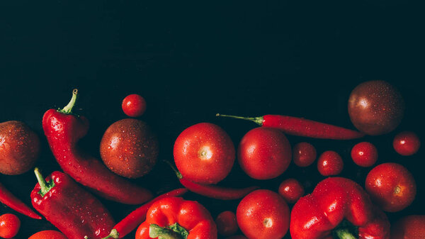 top view of red tomatoes, bell peppers and chili peppers on grey dark table