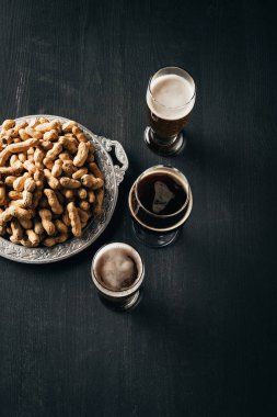 top view of arrangement of mugs of beer and peanuts on metal tray on dark wooden tabletop clipart