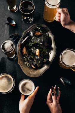 partial view of friends with glasses of beer at tabletop with mussels in bowl clipart