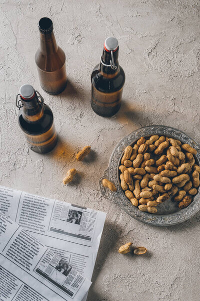 top view of peanuts, newspapers and bottles of beer arranged on concrete tabletop