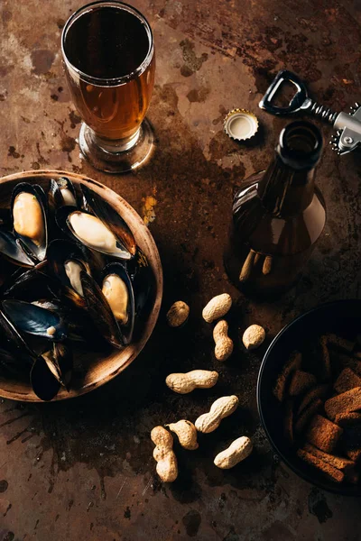 flat lay with beer, baked breads, mussels in bowl and peanuts on rust surface