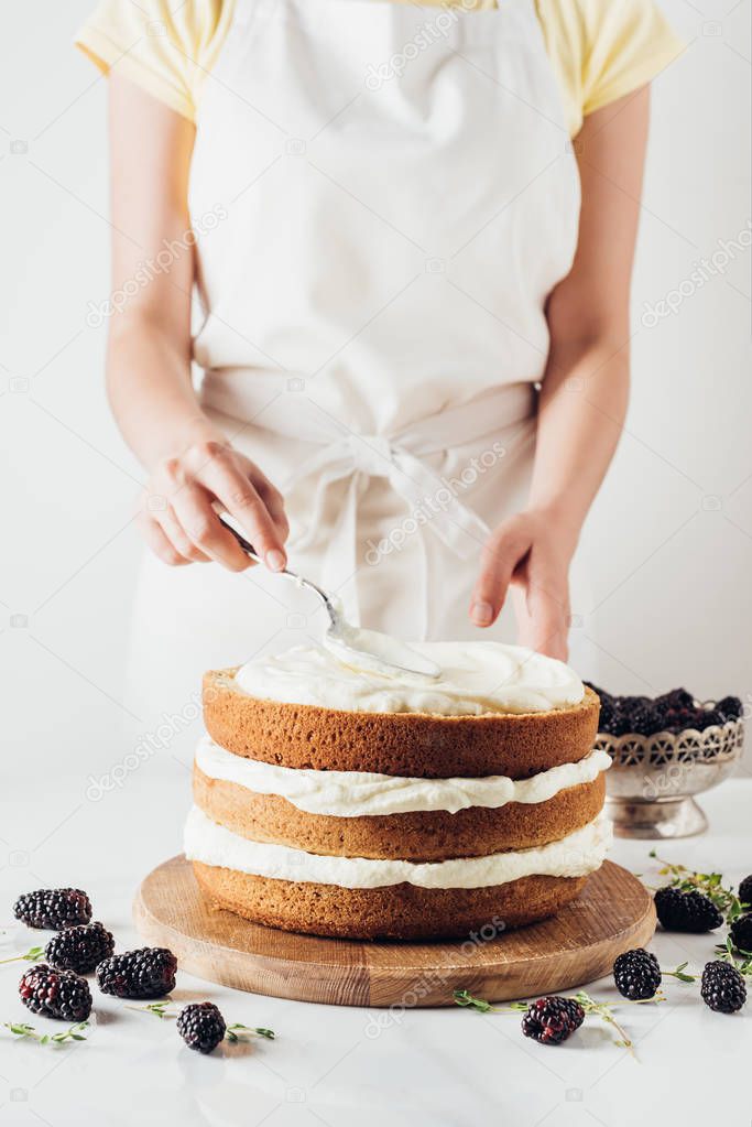 cropped shot of woman applying cream onto freshly baked cake on white