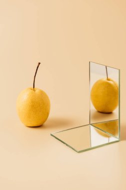 organic yellow pear reflecting in two mirrors on beige table clipart