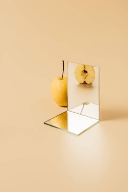 appetizing yellow pear reflecting in two mirrors on beige table clipart