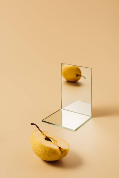one yellow pear reflecting in two mirrors on beige table