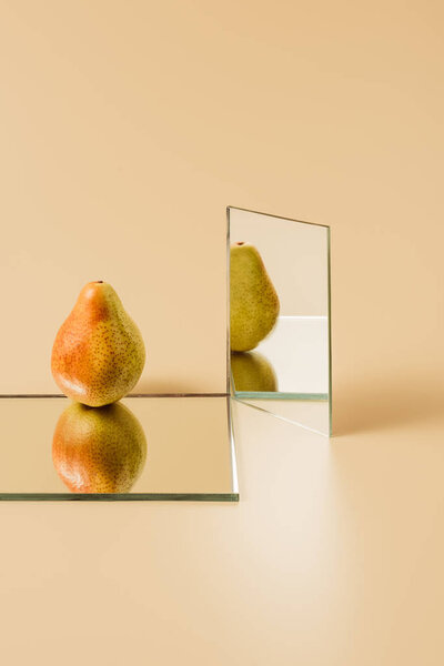 tasty pear reflecting in two mirrors on beige table 