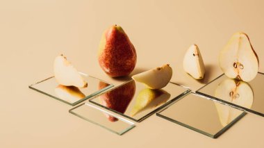 yellow pears reflecting in mirrors on beige table clipart